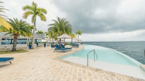 Área de piscina com espreguiçadeiras e palmeiras, com vista para o mar.