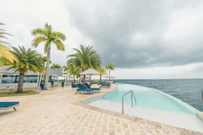 Ein Poolbereich mit Liegestühlen und Palmen, mit Blick auf das Meer.
