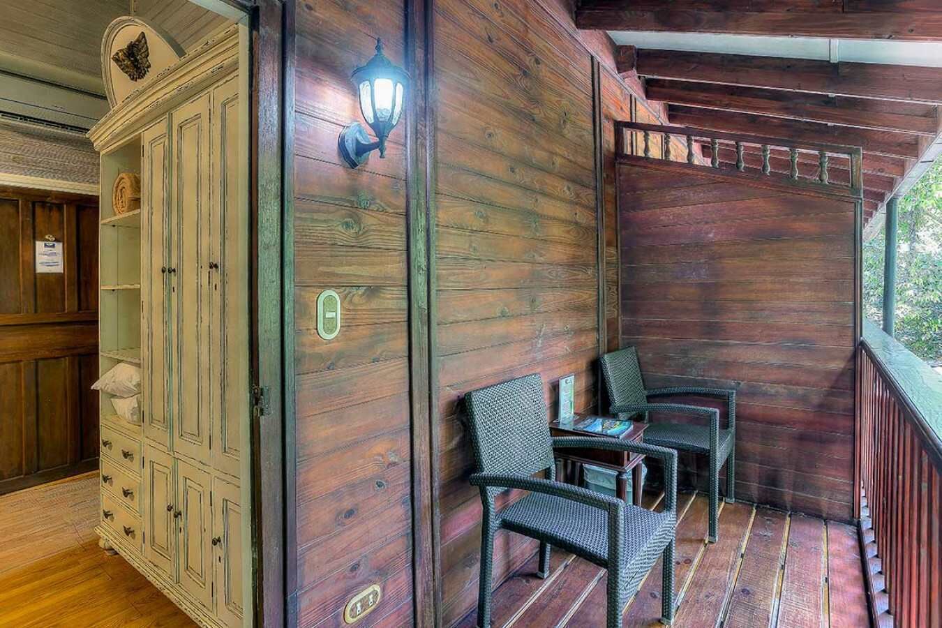 A wooden cabin with a porch, a cabinet with drawers, and two wicker chairs.