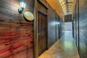 A hallway with wooden walls and doors, a tiled floor, and a light fixture on the wall.