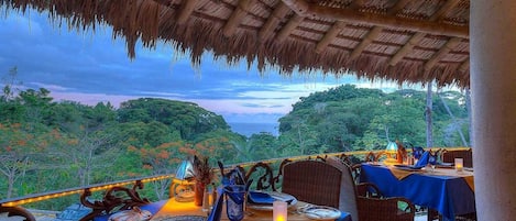 An outdoor dining area with tables set for two, overlooking a lush landscape.