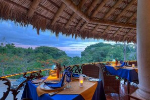 An outdoor dining area with tables set for two, overlooking a lush landscape.