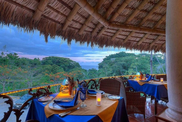 An outdoor dining area with tables set for two, overlooking a lush landscape.