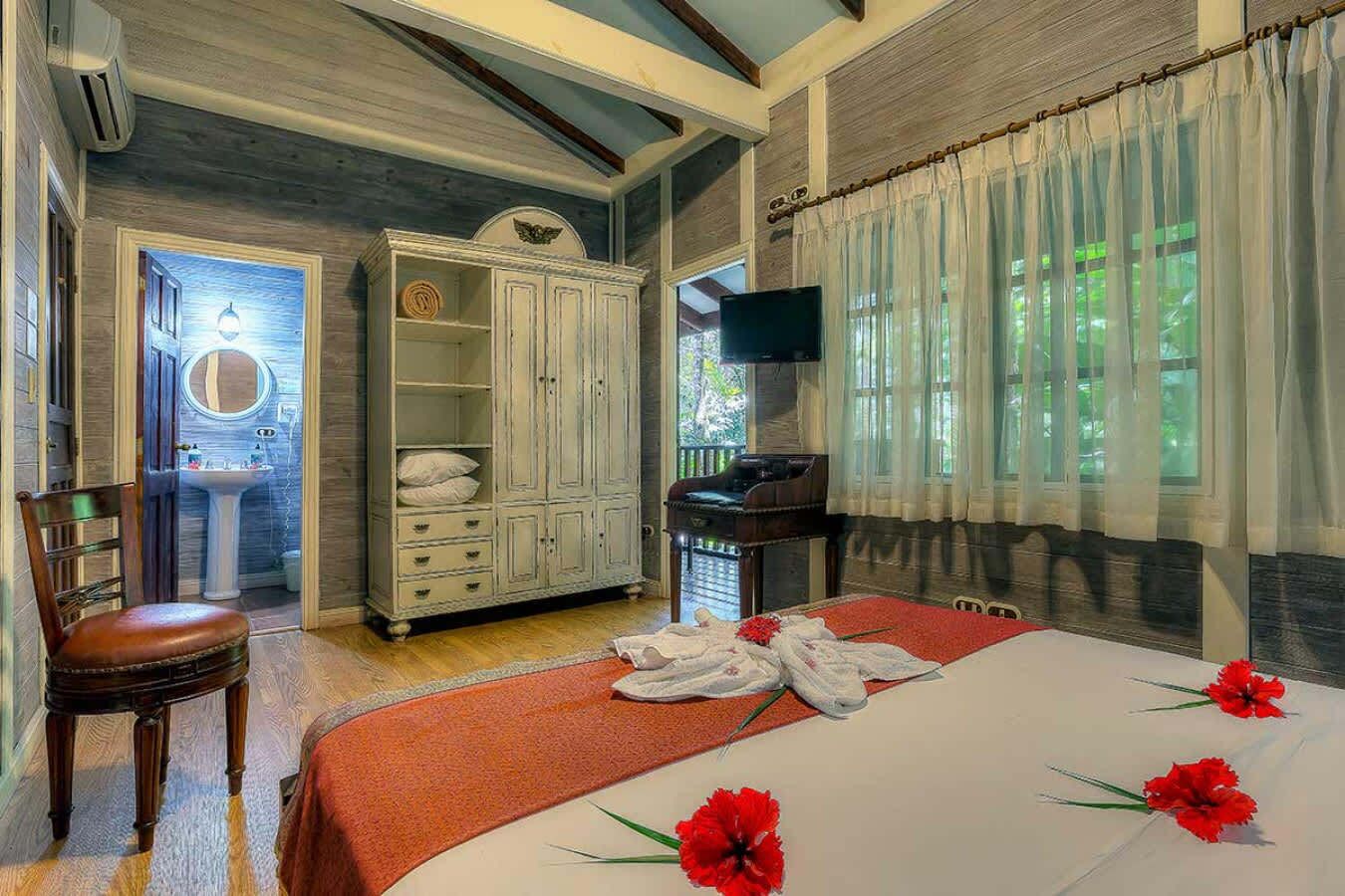 A bedroom with a bed, a wardrobe, a television, and a bathroom with a sink and mirror.