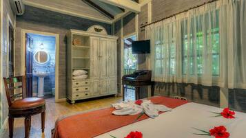 A bedroom with a bed, a wardrobe, a television, and a bathroom with a sink and mirror.