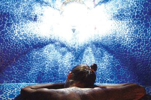 A person sitting in a bathtub with a mosaic tile wall.
