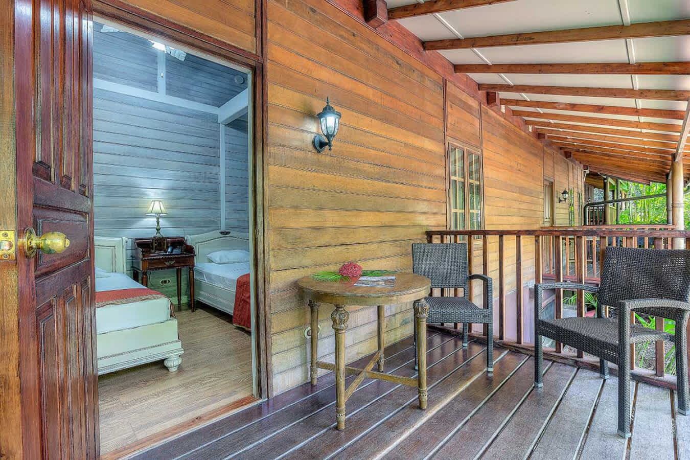 A wooden cabin with a porch, a bed, a table with a flower, and wicker chairs.