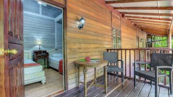 A wooden cabin with a porch, a bed, a table with a flower, and wicker chairs.