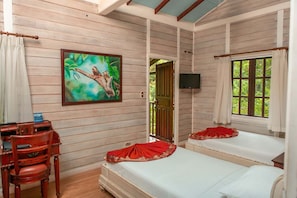 A room with two beds, a desk, a chair, a painting, a television, and a window with curtains.