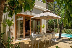 A wooden deck with a table and chairs, a pool, and a covered area with an umbrella. - The Spice Island Grand Estate (Paje)