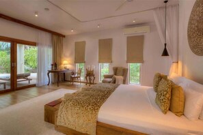 A spacious bedroom with a large bed, a desk, and two chairs. - The Spice Island Grand Estate (Paje)