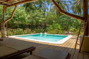 Uma piscina retangular com um deck de madeira ao redor, situada num exuberante jardim tropical com palmeiras.