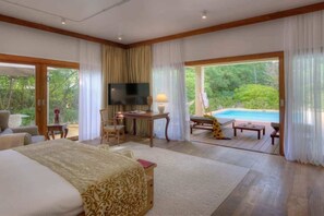 A spacious bedroom with a large bed, a desk, and a view of a swimming pool. - The Spice Island Grand Estate (Paje)