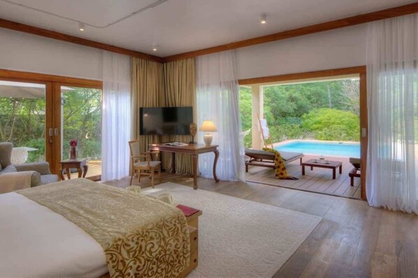 Un dormitorio amplio con una cama grande, un escritorio y vistas a una piscina.