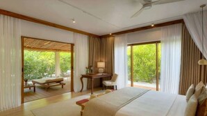 A bedroom with a large bed, a desk, and a chair, with a view of greenery outside. - Eco-Luxury Pool Villa (Paje)