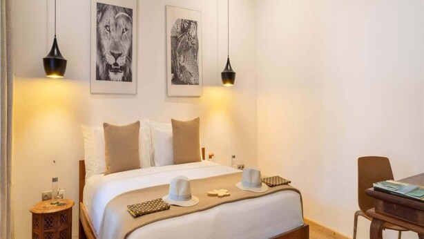 Et hotelværelse med en seng, to væglamper, et lille trænatbord og en stol.