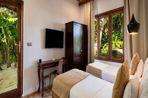 Ein Hotelzimmer mit zwei Betten, einem Fernseher, einem Schreibtisch und einem Fenster mit Blick auf Grünflächen.