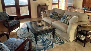 Sala de estar com sofá, cadeiras, mesa de centro e vista através de uma porta de vidro.