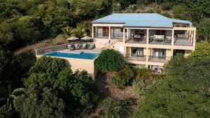 Uma casa de dois andares com piscina, cercada por vegetação densa.