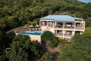 A two-story house with a swimming pool, surrounded by dense greenery. - Beneath the Mango Tree: Private Pool, Prime Location, Stunning Sunsets! (Cruz Bay)
