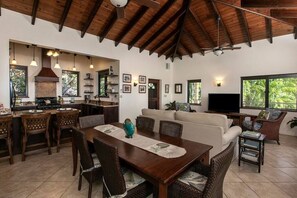 A spacious living area with a dining table, sofas, and a television. - Beneath the Mango Tree: Private Pool, Prime Location, Stunning Sunsets! (Cruz Bay)