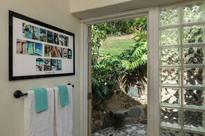 A framed collage of nature photos on a wall, a door leading to a garden, and a window with a stone wall view. - Beneath the Mango Tree: Private Pool, Prime Location, Stunning Sunsets! (Cruz Bay)