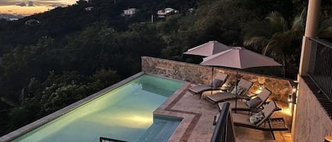Ein Schwimmbecken mit Steinbord, Liegestühlen und Sonnenschirmen.