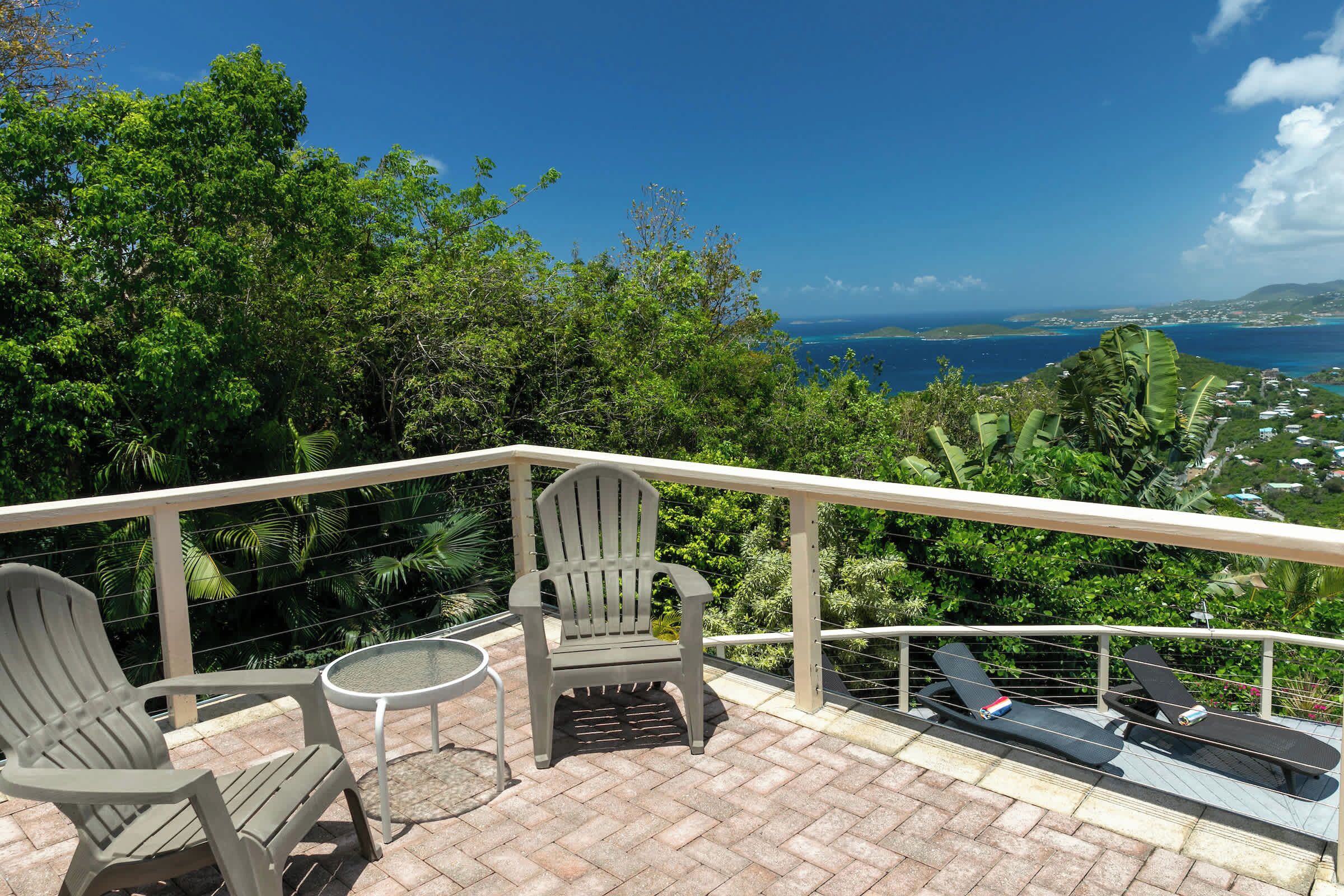 A balcony with two Adirondack chairs, a small round table, and a sun lounger.