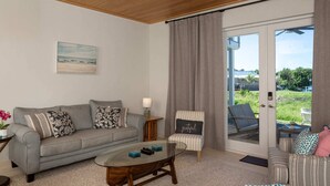 Una sala de estar con un sofá gris, un sillón a rayas, una mesa de centro de vidrio y vistas a través de un ventanal corredero.