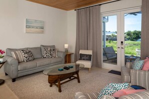 Ein Wohnzimmer mit grauem Sofa, einem gestreiften Sessel, einem Glastisch und Blick durch eine Schiebetür.