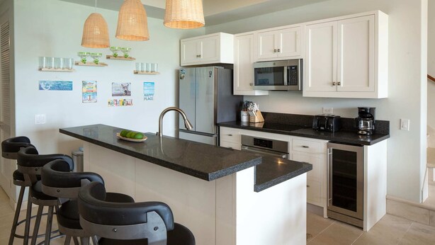 Una cocina moderna con armarios blancos, una isla central con taburetes de bar, un refrigerador, un microondas y una cafetera.