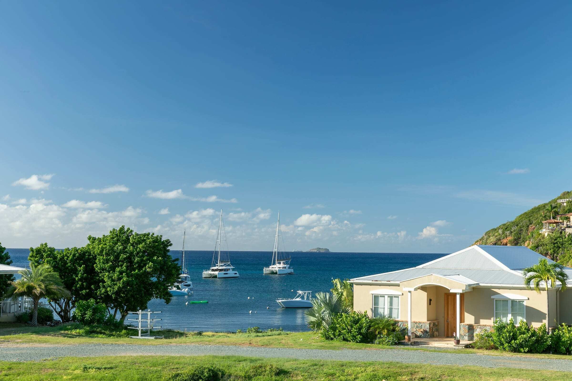 A coastal property with a house, a grassy area, and sailboats on the water.