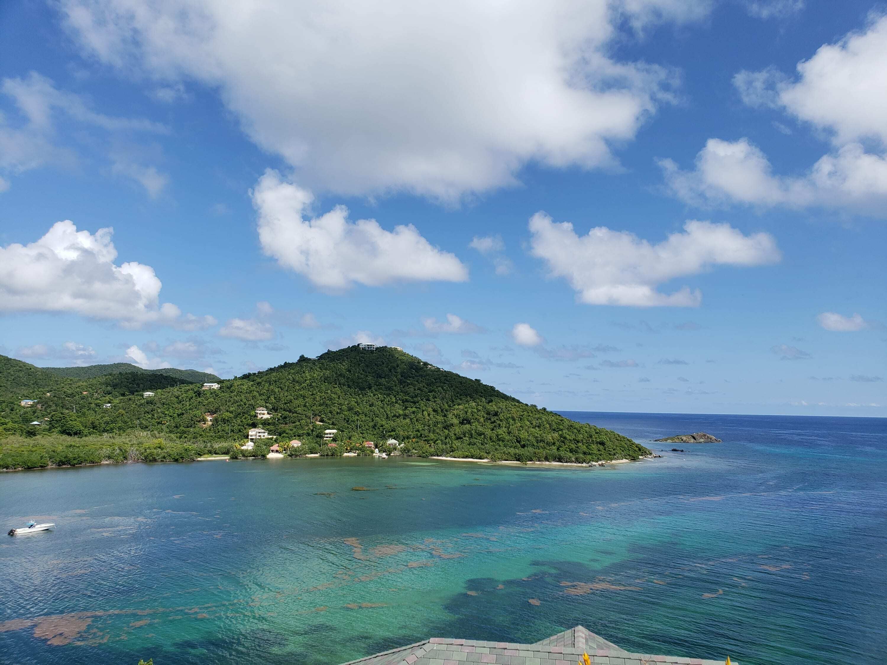A coastal landscape with a small island, clear blue waters, and a few buildings on the island.