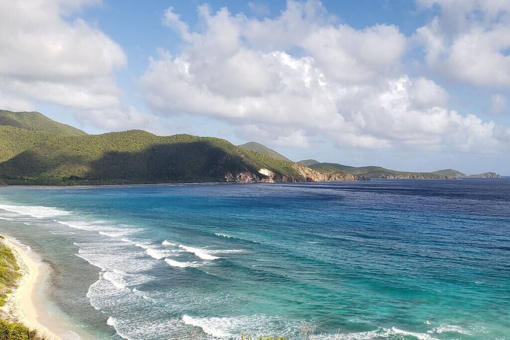 Eine Küstenlandschaft mit Strand, Meer und grünen Hügeln.