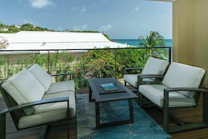 A balcony with two white cushioned chairs, a small table, and a view of the ocean and greenery. - Nautilus-Beach Front, Family Friendly, Prime Locale (Cruz Bay)