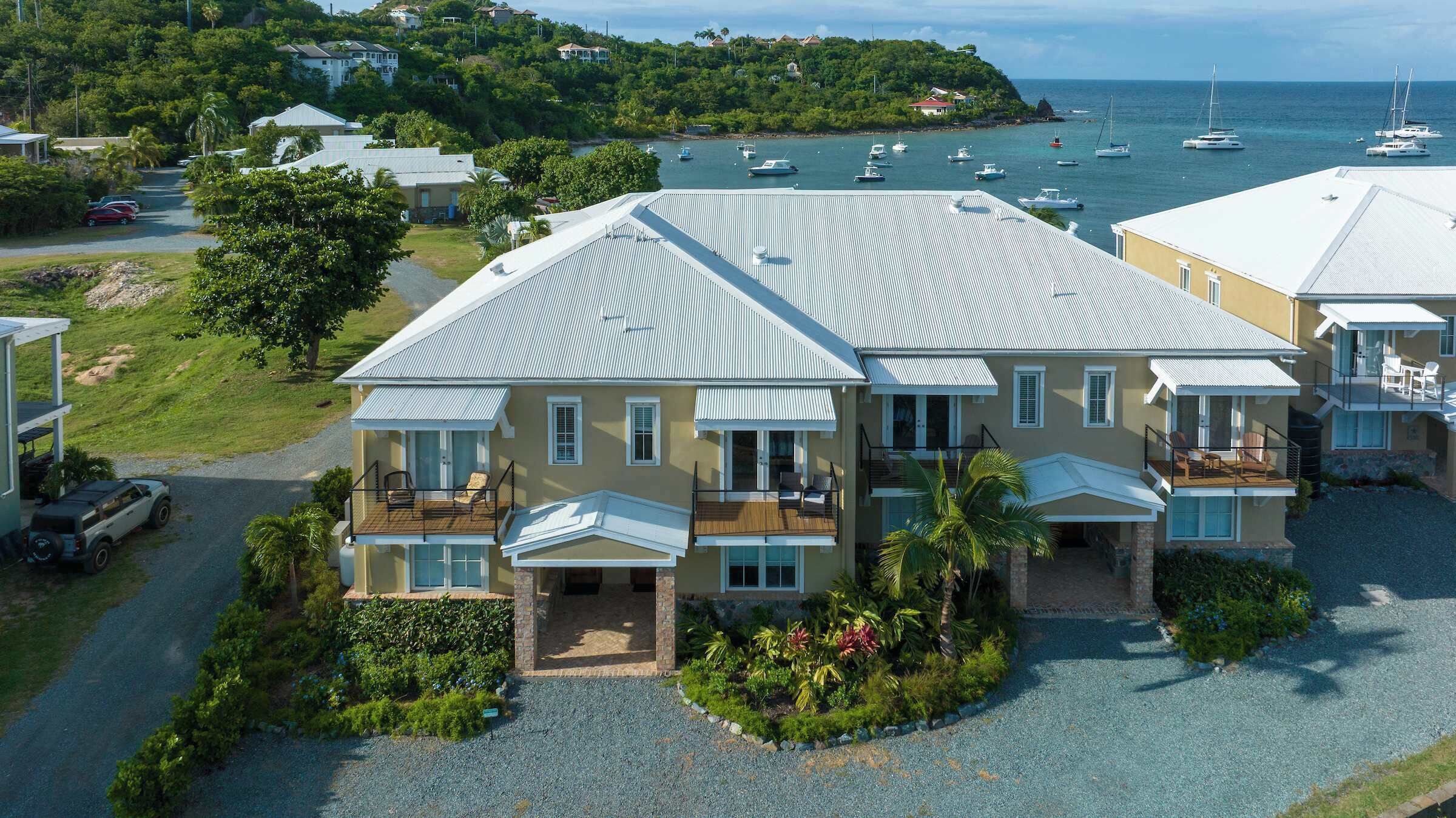 A two-story house with a balcony, a driveway, and a view of the sea with boats.