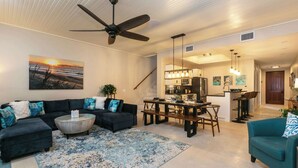 A spacious living room with a dark-colored sofa set, a coffee table, and a blue patterned rug. A dining area with a wooden table and chairs is visible in the background. - Serenity Villa- Steps from Beach, Family Friendly (Cruz Bay)