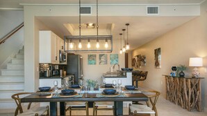 A dining area with a wooden table set for four, surrounded by chairs. A kitchen is visible in the background with modern appliances. - Serenity Villa- Steps from Beach, Family Friendly (Cruz Bay)