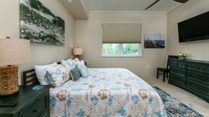 A bedroom with a bed, a dresser, a television, a ceiling fan, and a window with blinds. - Serenity Villa- Steps from Beach, Family Friendly (Cruz Bay)
