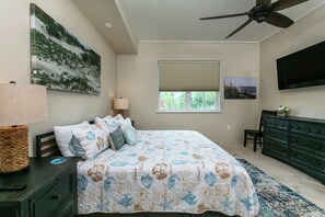 Ein Schlafzimmer mit Bett, Kommode, Fernseher, Deckenventilator und einem Fenster mit Jalousien.