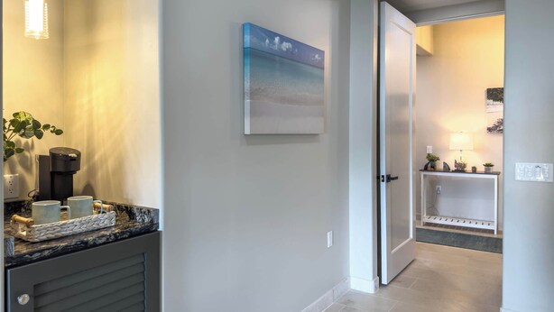 A hallway with a coffee machine, two mugs, a plant, and a painting on the wall. - Serenity Villa- Steps from Beach, Family Friendly (Cruz Bay)