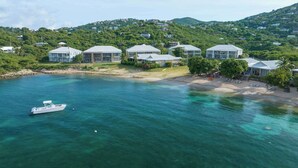 A coastal property with multiple houses, a boat docked near the shore, and a clear view of the surrounding greenery and hills. - Serenity Villa- Steps from Beach, Family Friendly (Cruz Bay)