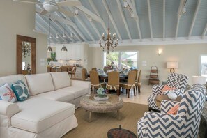 A spacious living room with a high ceiling, a dining area with a chandelier, and a kitchen in the background. - Maria Bluff Main House- Modern Renovations, Private Pool, Ocean Front Views, and Pool Table! (Cruz Bay)