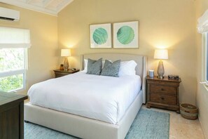 A bedroom with a bed, two bedside tables, a nightstand, a lamp, and artwork on the wall. - Maria Bluff Main House- Modern Renovations, Private Pool, Ocean Front Views, and Pool Table! (Cruz Bay)