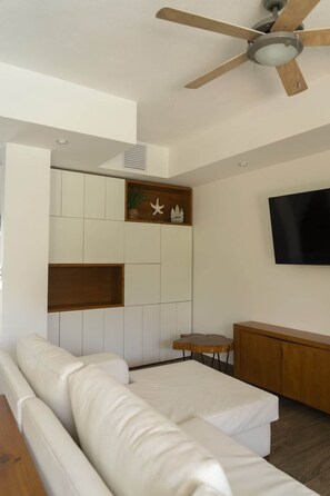 Un dormitori modern amb un sofà blanc, un armari de fusta, una televisió i un ventilador de sostre.