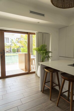 Una cucina moderna con una grande isola, sgabelli di legno e vista su piscina e vegetazione.