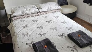 A neatly made bed with a patterned duvet, pillows, and folded towels. - Studio Sleeps 2 Near Station & Airport (Bishop's Stortford)