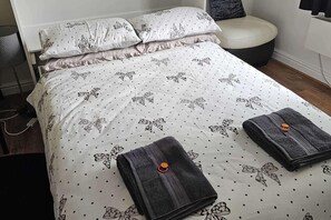 A neatly made bed with a patterned duvet, pillows, and folded towels. - Studio Sleeps 2 Near Station & Airport (Bishop's Stortford)