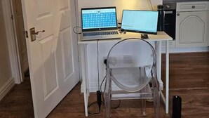 A room with a desk, two laptops, a clear plastic chair, and a white door. - Studio Sleeps 2 Near Station & Airport (Bishop's Stortford)