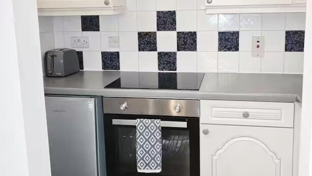 A compact kitchen with white cabinetry, a stainless steel refrigerator, a built-in oven, and a patterned backsplash. - Studio Sleeps 2 Near Station & Airport (Bishop's Stortford)